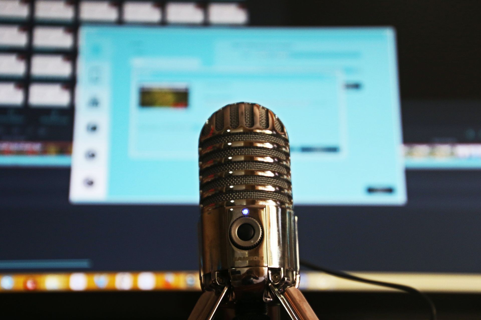 Close-up of a silver microphone in front of a blurred computer screen with editing software.